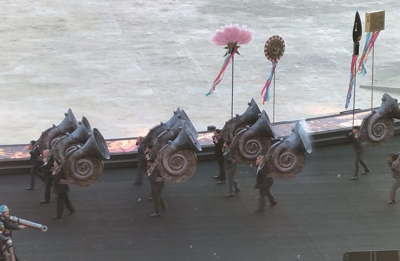 Performers in dark costumes carry large spiral props during a parade or celebration.